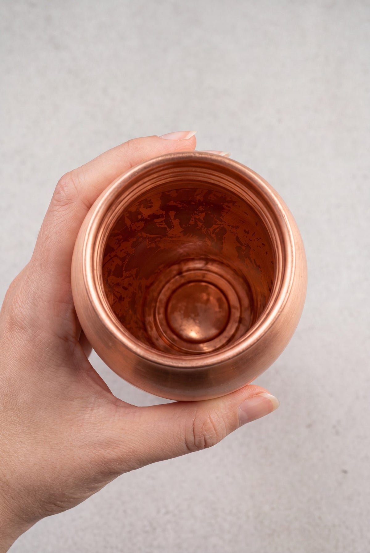 Een hand houdt een koperen waterfles schuin, met donkere vlekken op de binnenwand