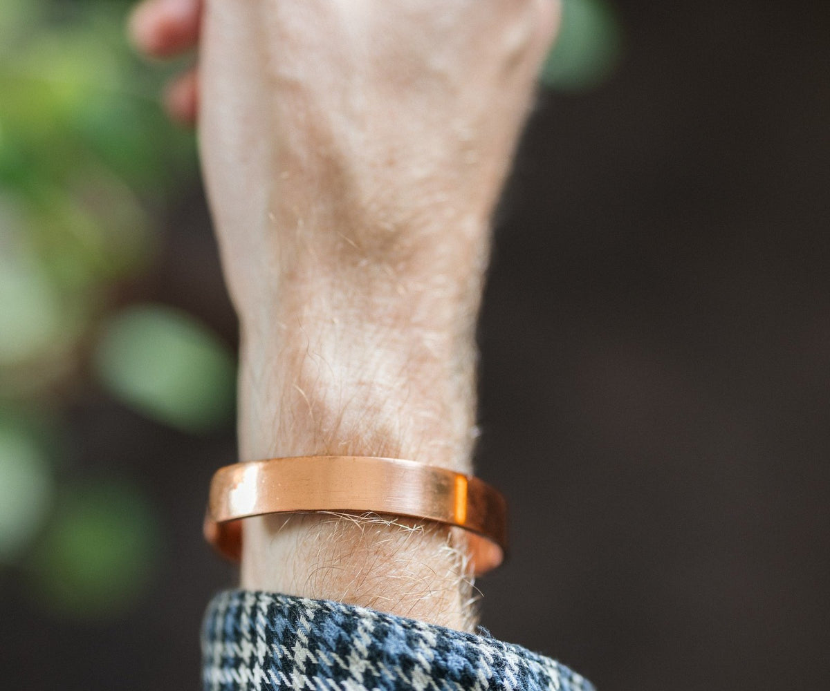 Kopero Koperen Armband Glad, om de pols, met de hand omhoog tegen een donkere achtergrond