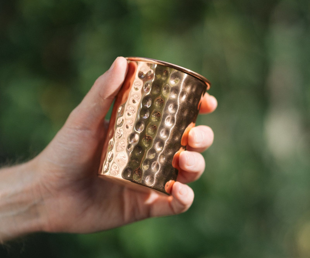 Kopero Koperen Beker Gehamerd, in een hand tegen een groene achtergrond