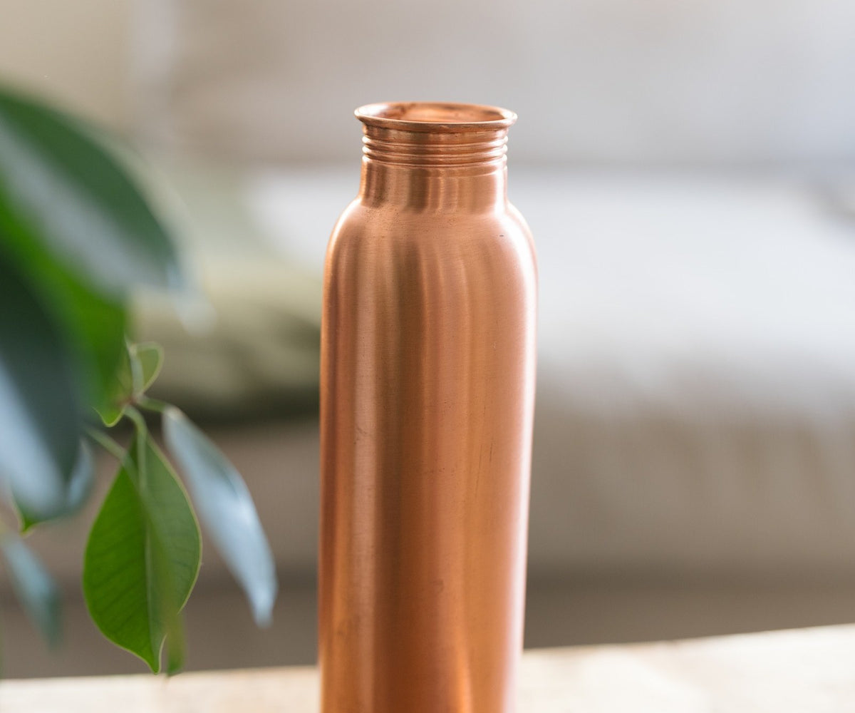Kopero Koperen Waterfles Glad, staand op een houten tafel voor een bank, met de losse dop ernaast