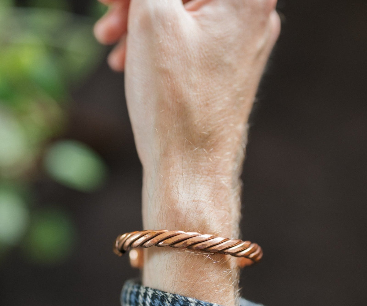Kopero Koperen Armband Gedraaid, om de pols, met de hand omhoog tegen een donkere achtergrond