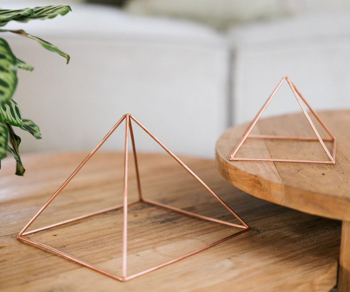 Twee gladde koperen piramides van verschillende grootte op een houten salontafel