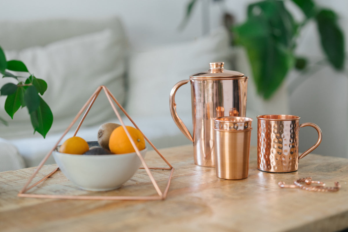 Koperen piramide, kan, beker, mok en armband samen op een houten tafel