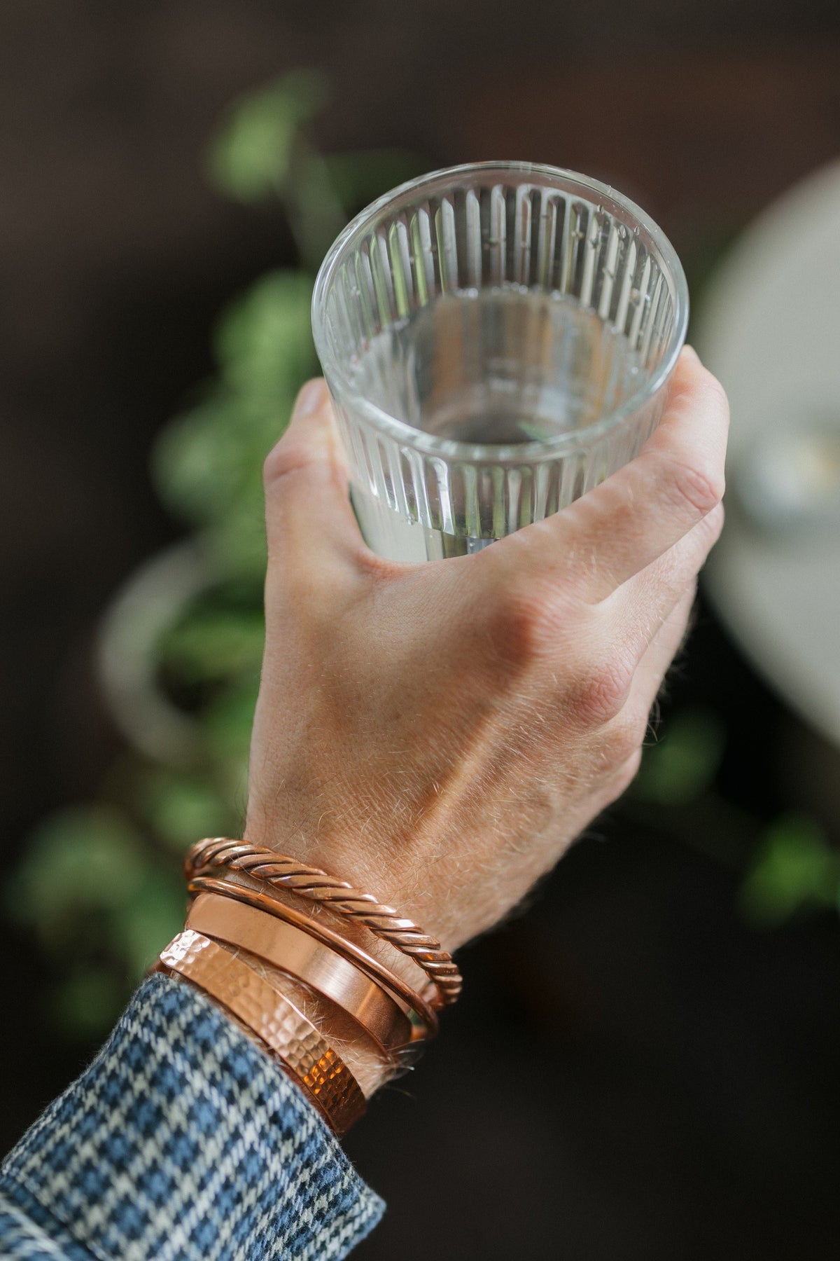 Kopero Koperen Armband, alle vier de uitvoeringen samen om één pols, met een glas water in de hand