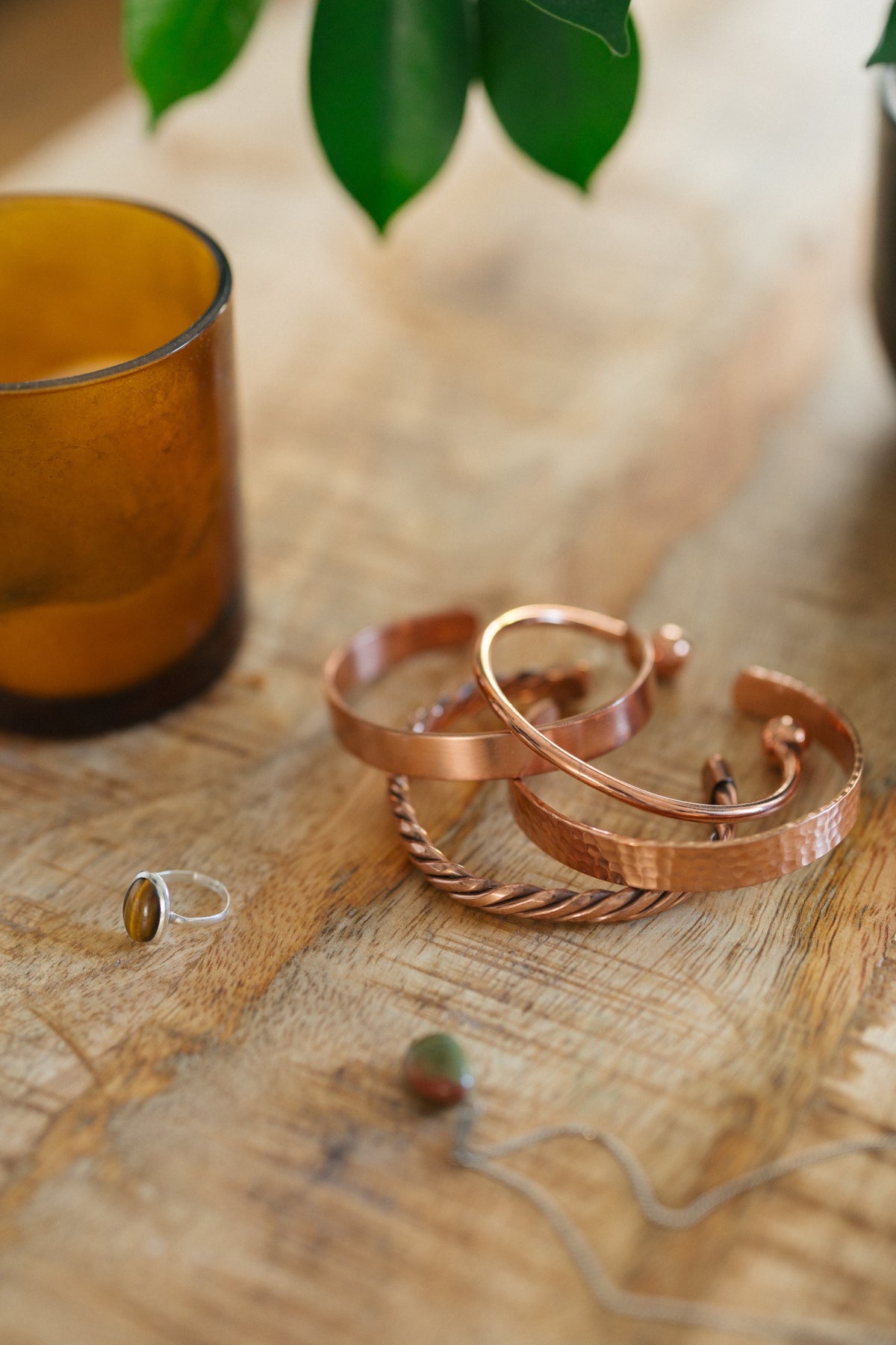 Kopero Koperen Armband, alle vier de uitvoeringen samen op een houten tafel met een kaars en een ring