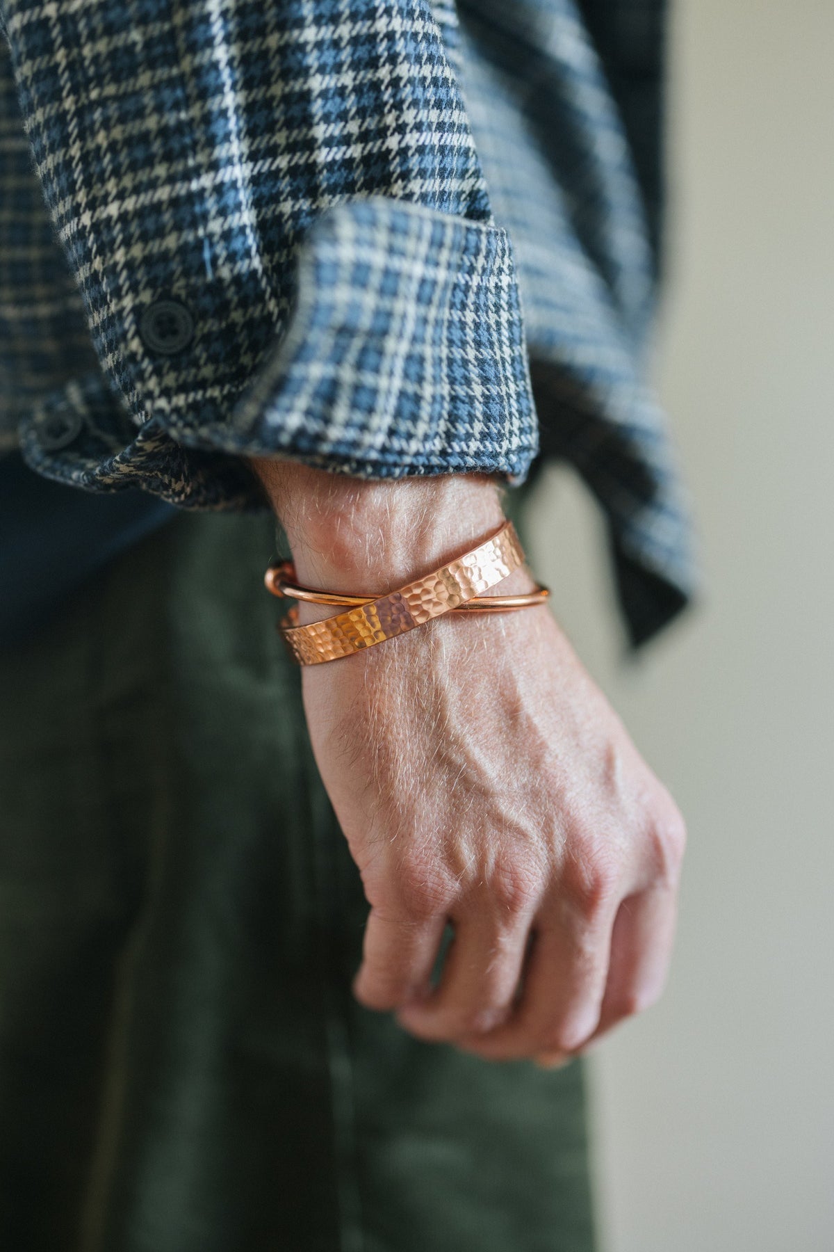 Kopero Koperen Armband Gehamerd, om de pols over een geruite overhemdsmouw, samen met een gladde armband