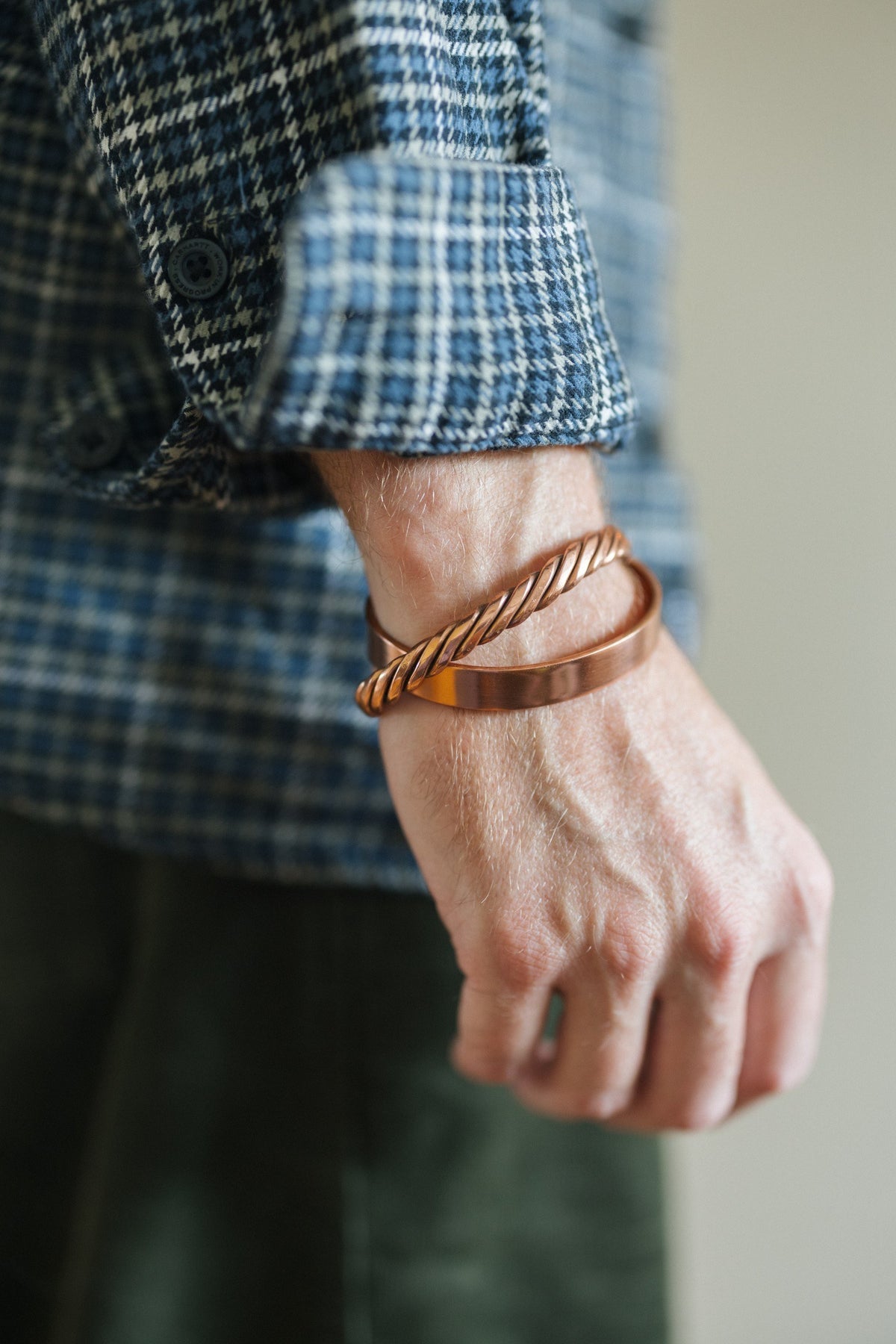 Kopero Koperen Armband Glad, om de pols over een geruite overhemdsmouw, samen met een gedraaide armband