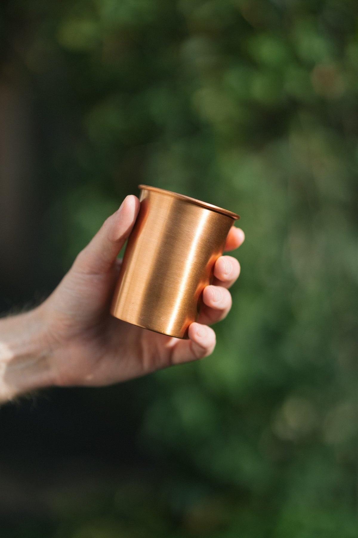 Kopero Koperen Beker Glad, in een hand tegen een groene achtergrond