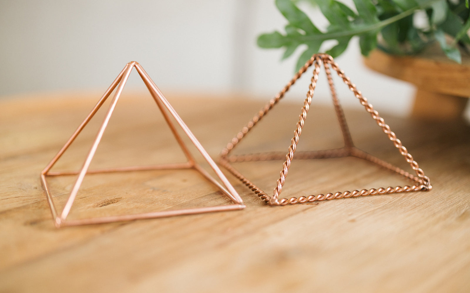 Twee koperen piramides, gedraaid en glad, naast elkaar op een houten tafel