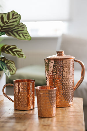 Kopero Koperen Kan Gehamerd, met een mok en een beker op een houten tafel