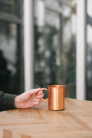 Kopero Koperen Mok Glad, op een houten tafel, met een hand aan het handvat