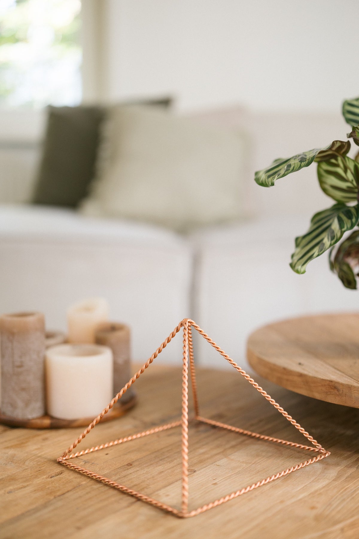Kopero Koperen Piramide Energizer Gedraaid Groot (23,56 cm), op een houten salontafel voor een bank, naast kaarsen