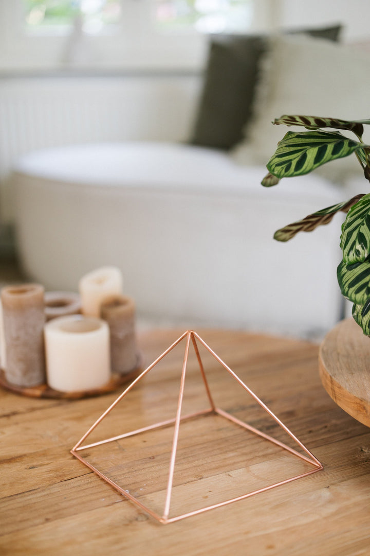 Kopero Koperen Piramide Energizer Glad Groot (23,56 cm), op een houten salontafel voor een bank, naast kaarsen