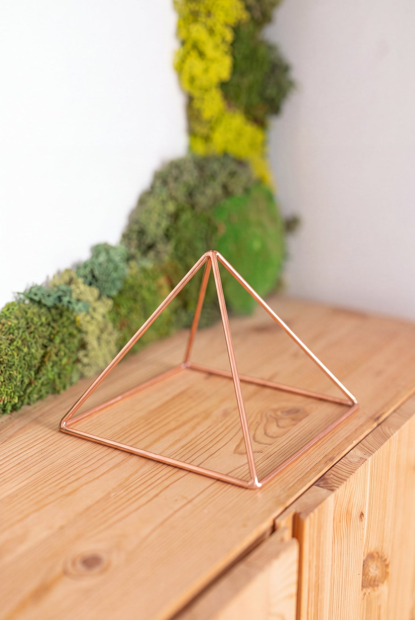 Kopero Koperen Piramide Energizer Glad Klein (14,56 cm) op een grenen kast voor een mosschilderij