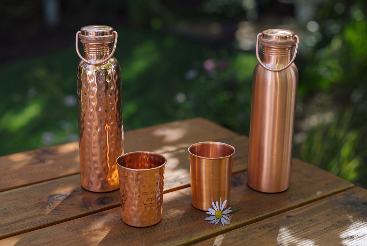 Koperen waterflessen, gladde en gehamerde bekers en een madeliefje op een houten tuintafel