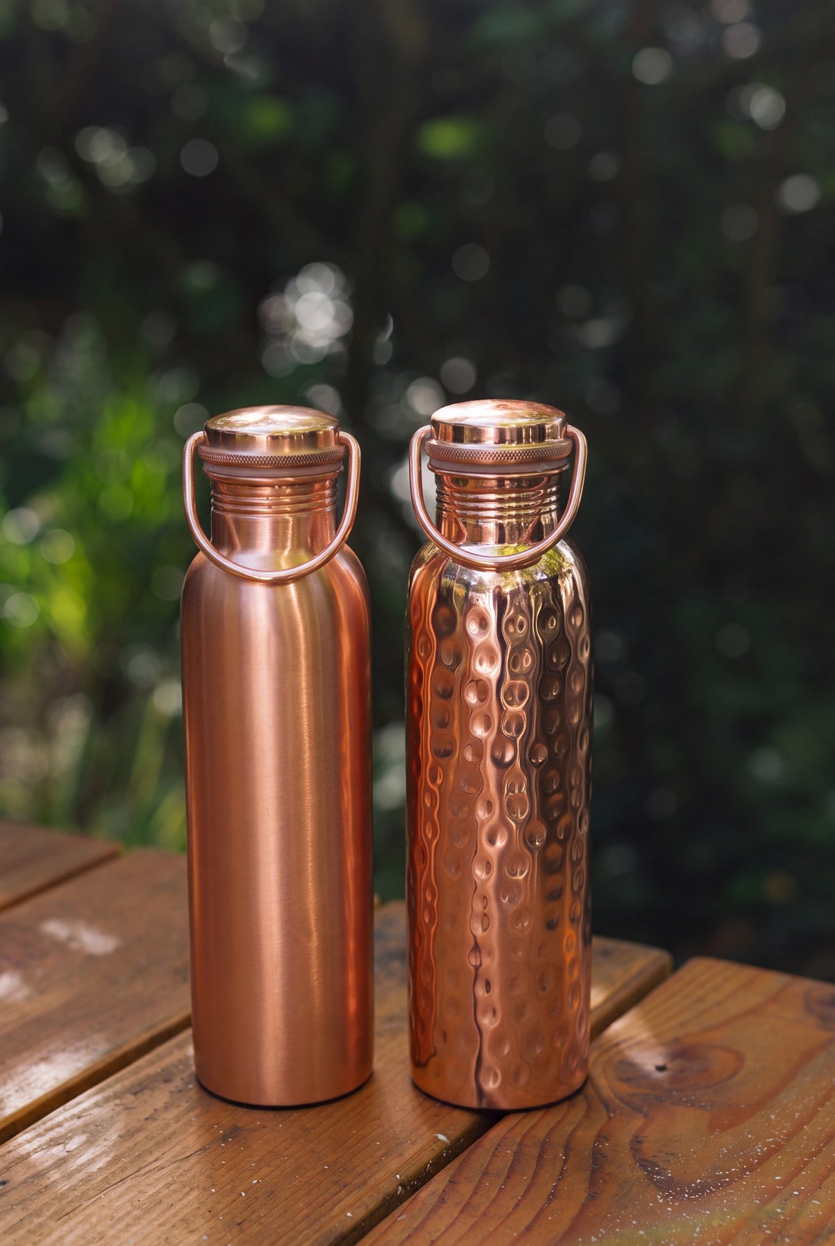 Kopero Koperen Waterfles, de gladde en de gehamerde fles naast elkaar op een houten tuintafel