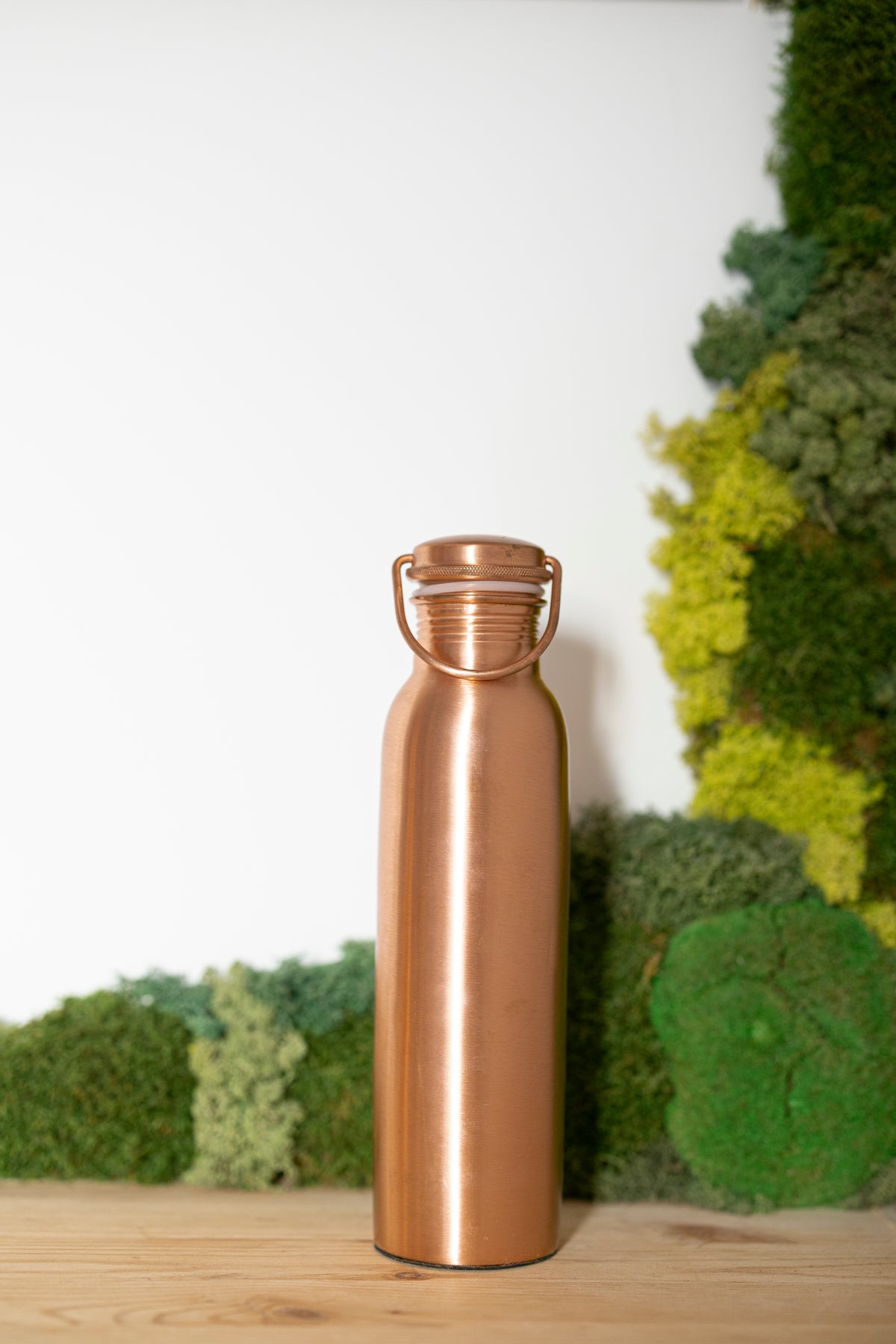 Kopero Koperen Waterfles Glad, 900 ml, rechtop op een houten tafel voor een mosachtergrond