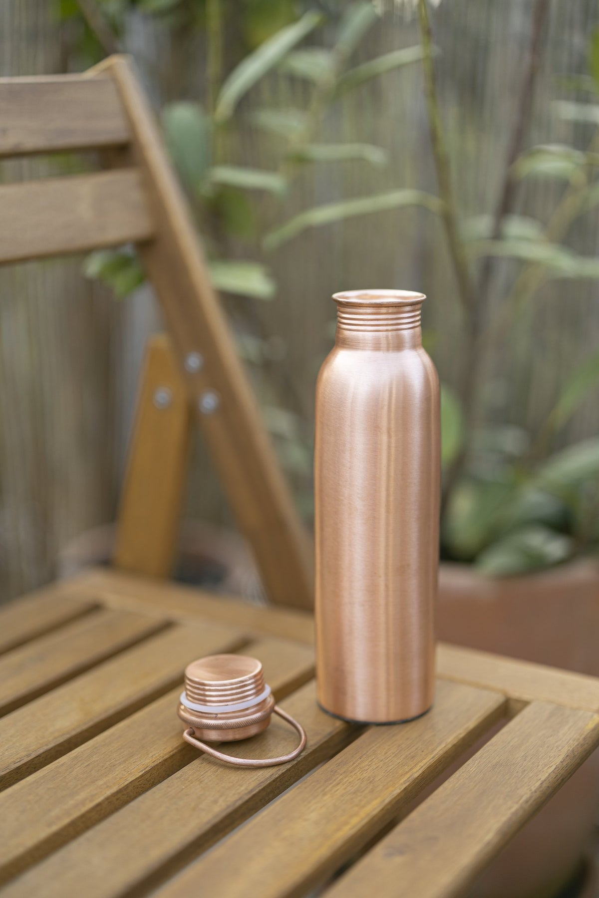 Kopero Koperen Waterfles Glad op een houten tuinstoel, met de dop ernaast