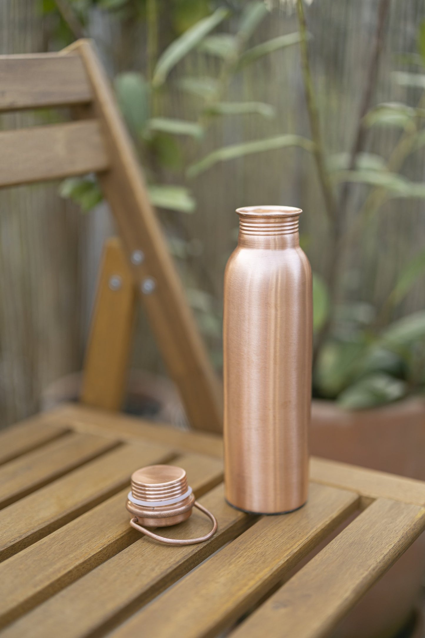 Kopero Koperen Waterfles Glad op een houten tuinstoel, met de dop ernaast