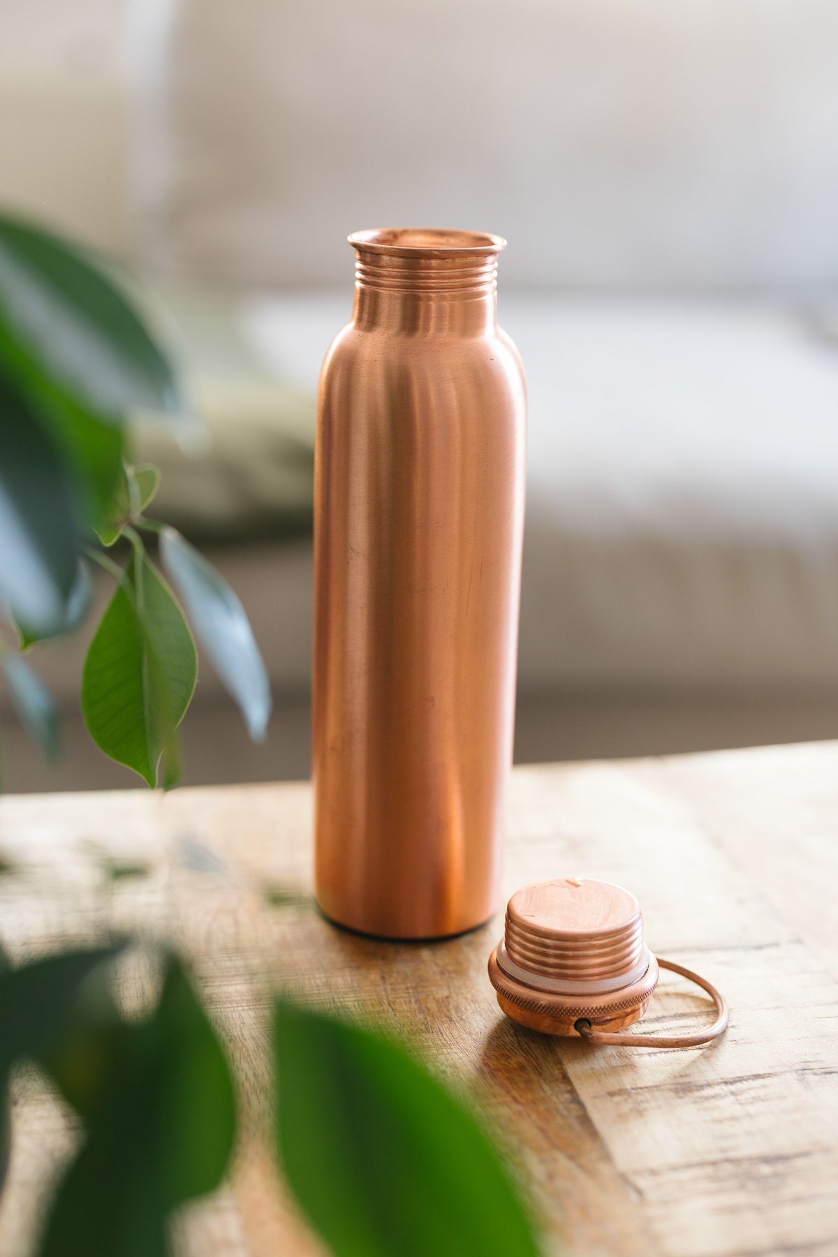 Kopero Koperen Waterfles Glad, staand op een houten tafel voor een bank, met de losse dop ernaast